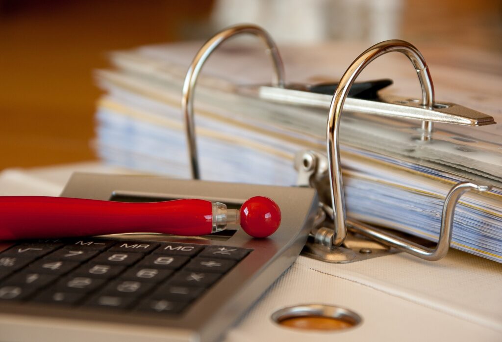 A pen and calculator sitting by a stack of papers.