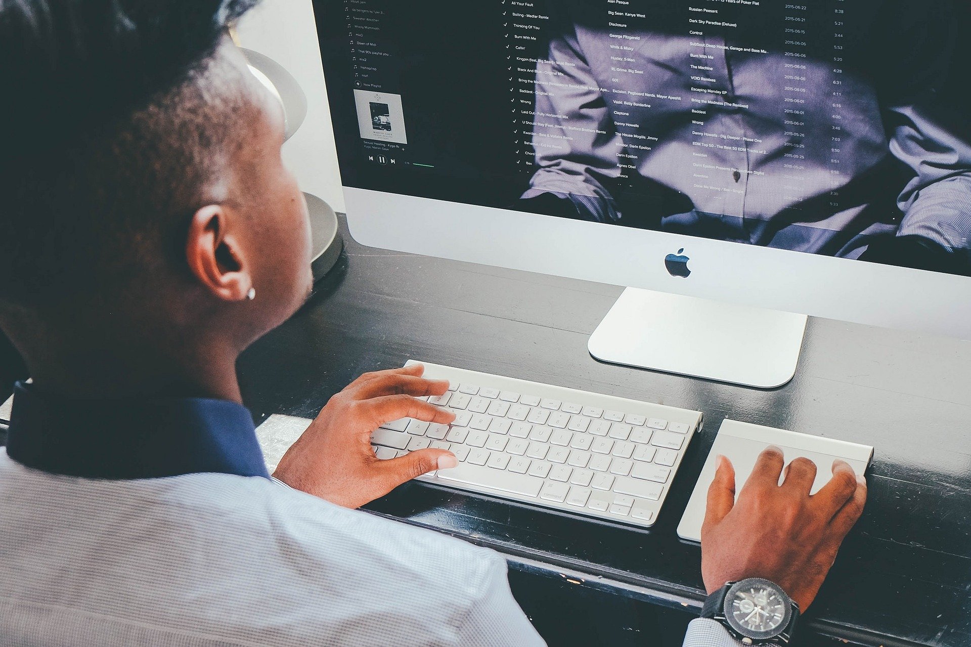 A black person with a short haircut sits at a computer looking through their email inbox.