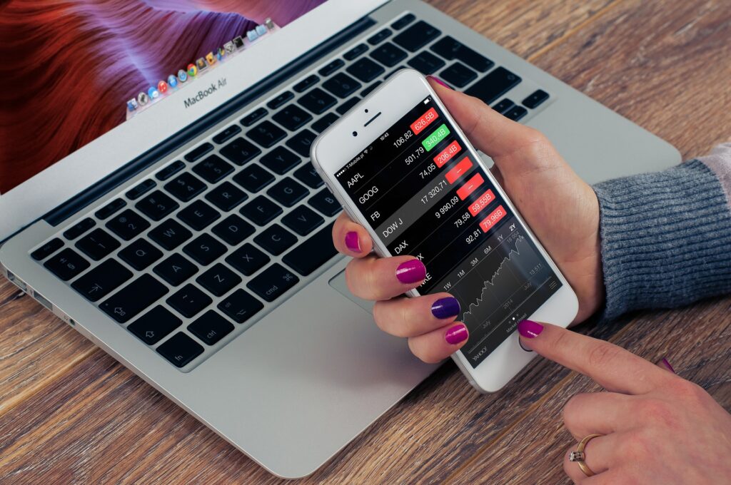 A white woman holding a cell phone with stock reports on the screen.