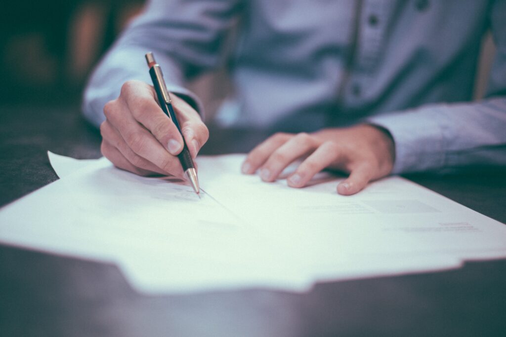 A white person visible from the waist to shoulders writing on papers.