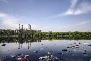 A river with garbage in it and a factory in the background.