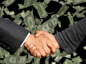 Two business associates shaking hands with dollar bills falling in the background.