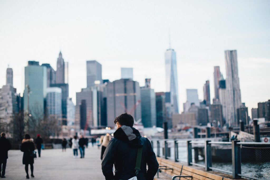 A view of people walking on a boardwalk with the skyline of the city in the background.