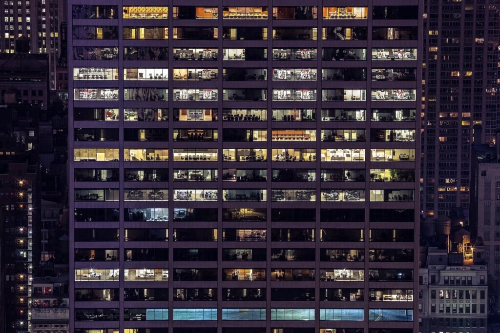 A view of an office building at night. The view allows for a look inside of the offices through the windows.