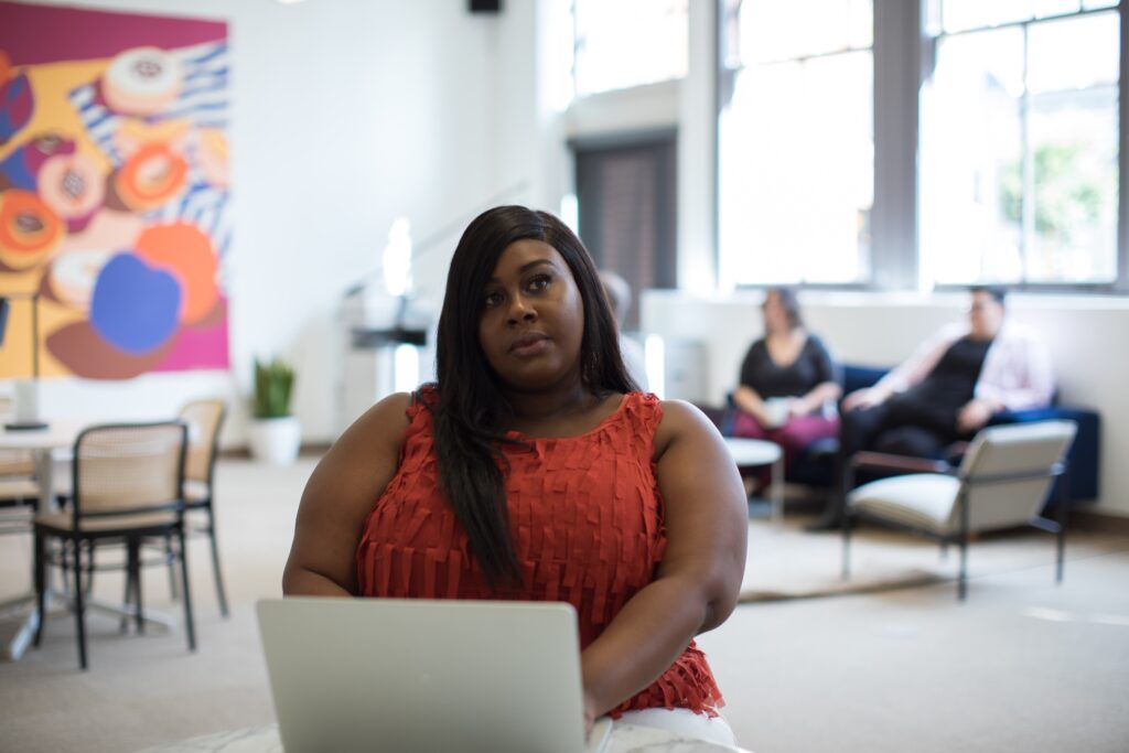 a plus sized black woman sitting at a table in front of a laptop.