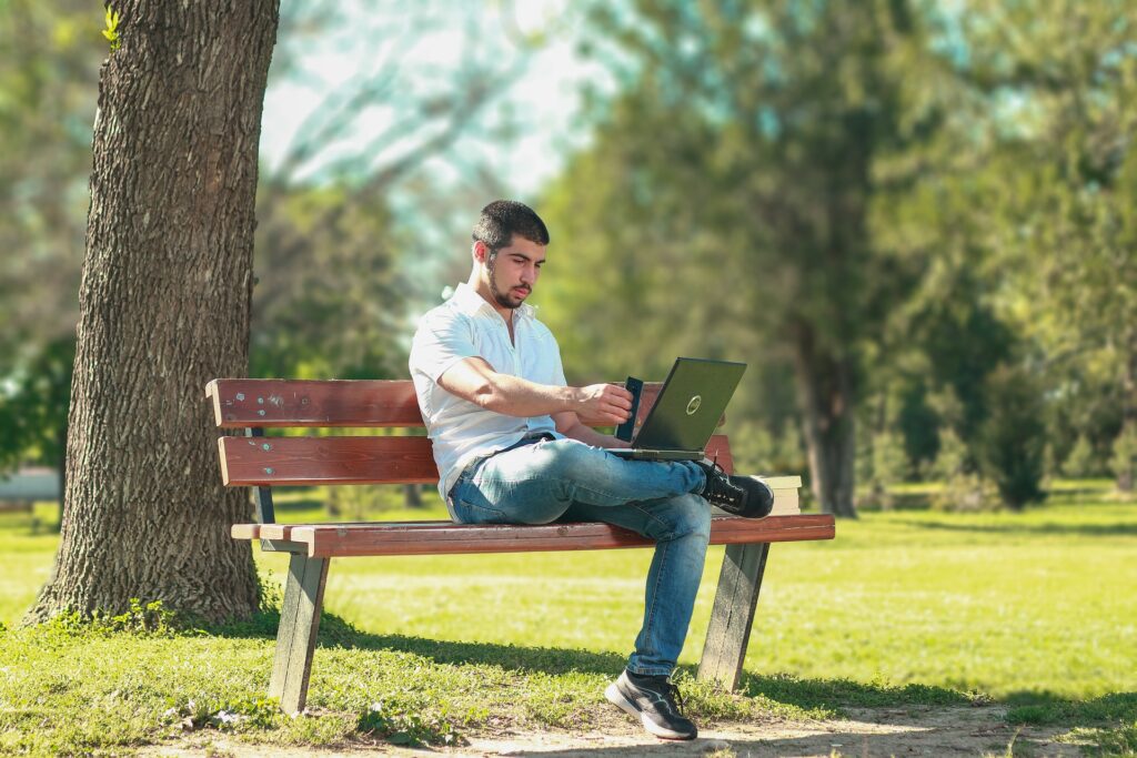 A man sitting at a park working on his latptop.