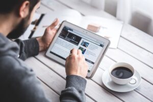 A man working on a tablet with papers and coffee on the table next to him.