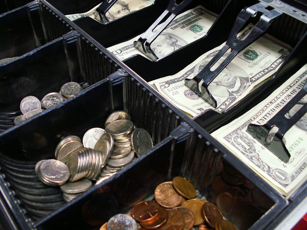 An open cash register drawer, filled with bills and coins of varying values.