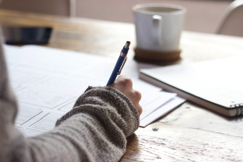 A white person writing on sheets of loose paper. Only their hand is shown.