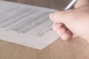 A person signing a piece of paper on the signature line.